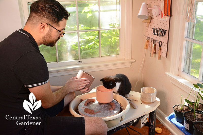 man at pottery wheel with black and white cat looking over 