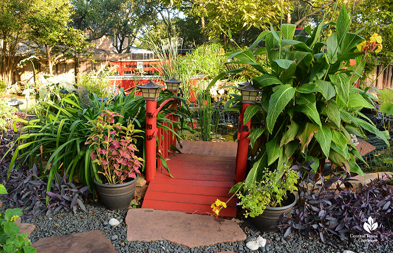 red arched bridge framed by plants Japanese characters on posts