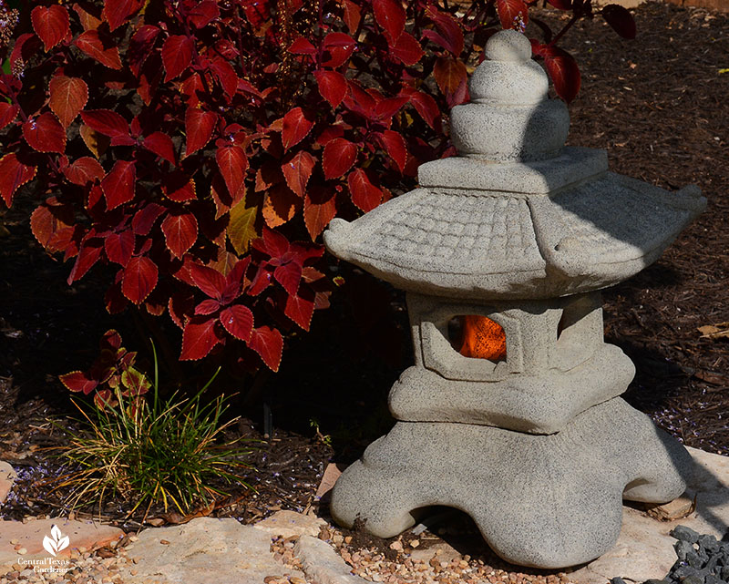 burgundy plant next to stone Japanese lantern with flame bulb 