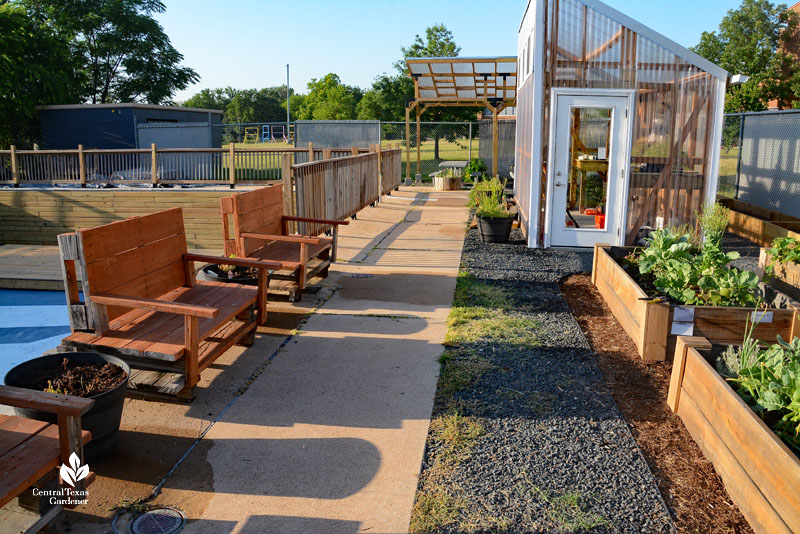 walkway with raised garden beds benches and greenhouse