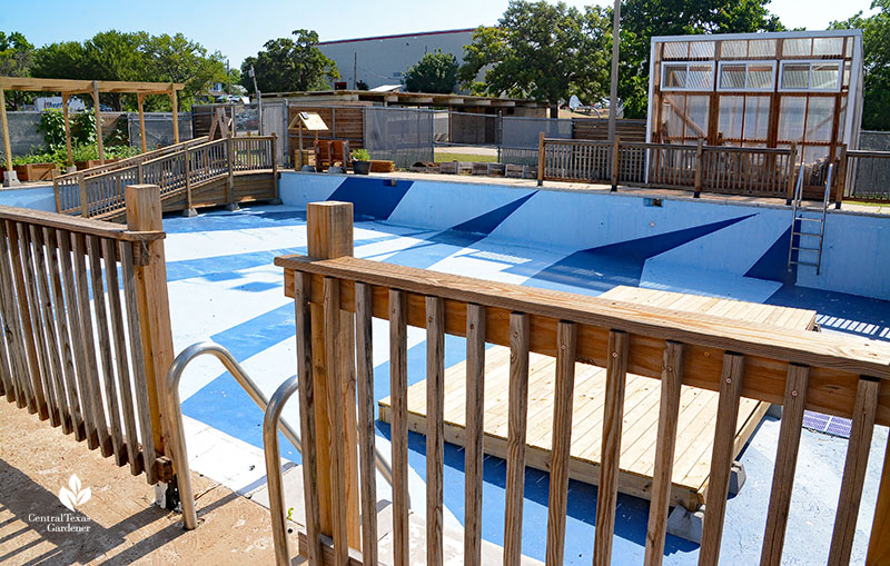 railing on empty swimming pool to greenhouse and raised beds