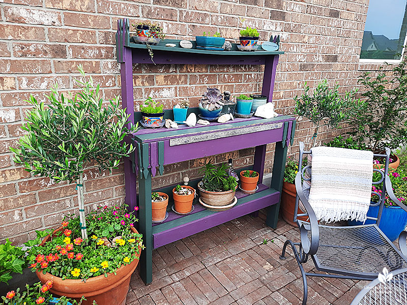 purple and sage green plant stand with containers and art