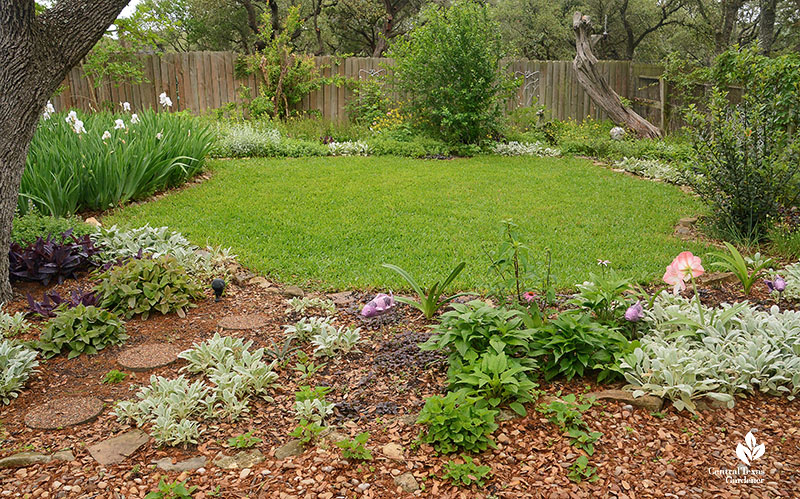 plants in border against river rock to grassy cove backed by fence and garden border