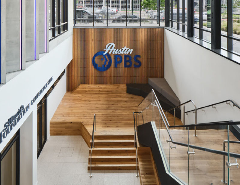 staircase to Austin PBS sign on wood paneled wall; windows above