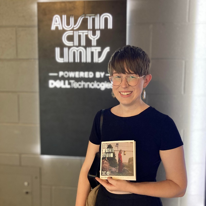 woman in front of Austin City limits sign and holding a program for the performance