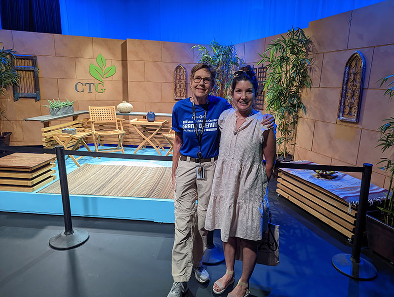 woman in blue Grand Opening T-shirt and smiliing woman in dress on CTG studio set