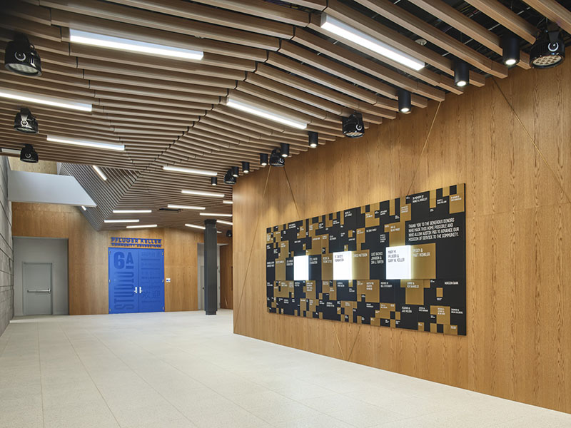 hallway with wood wall on one side with plaques and blue door at end of hall with words "Studio 6A Pfluger Keller"