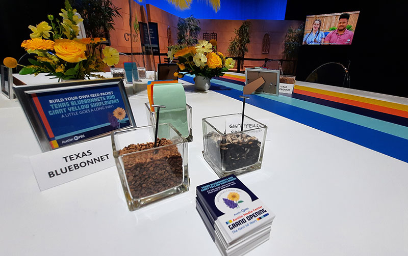 square glass containers filled with seeds on table; card noting "Bluebonnets" and a sign to make your own seed packets 
