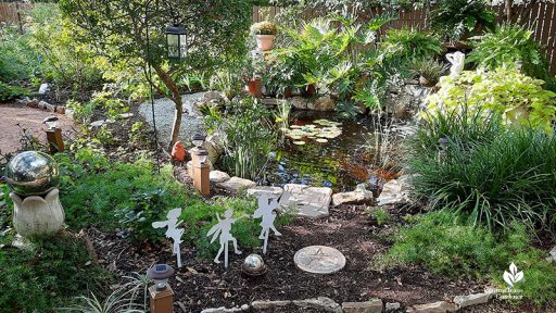 small backyard pond with plants and garden art all around it