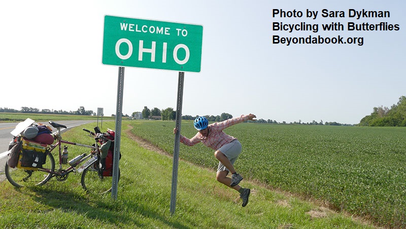 woman joyfully jumping up while holding post for Welcome to Ohio highway sign