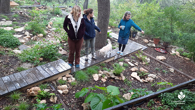 three woman and dog on backyard boardwalk looking at plants