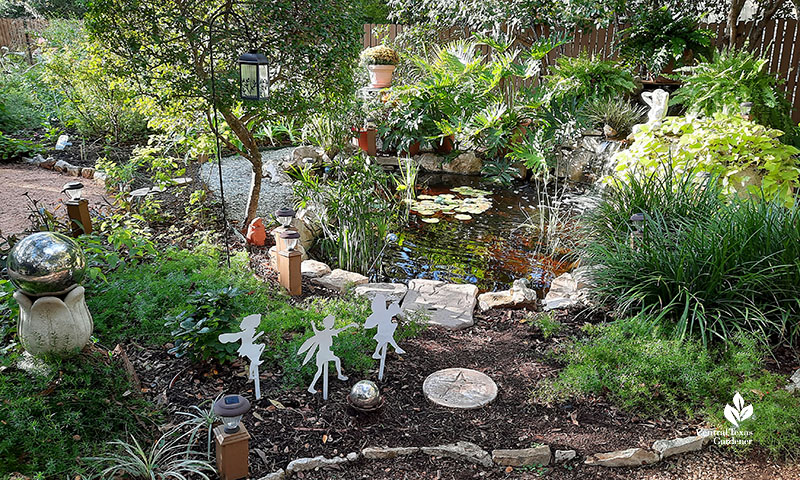 small pond bordered by plants and garden art including dancing sprites