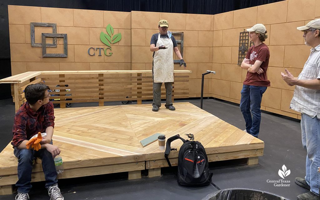 man standing on unpainted TV platform with other crew watching