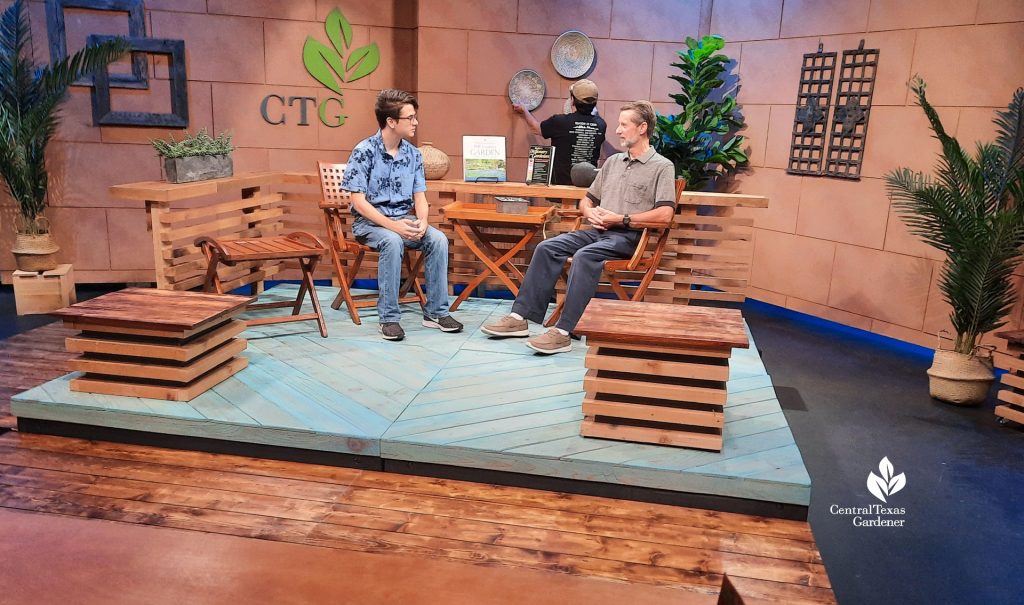 two men on studio set plaform while another arranges baskets on the wall