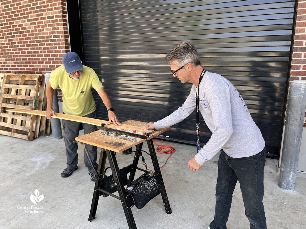 two men sawing lumber on portable worktable 
