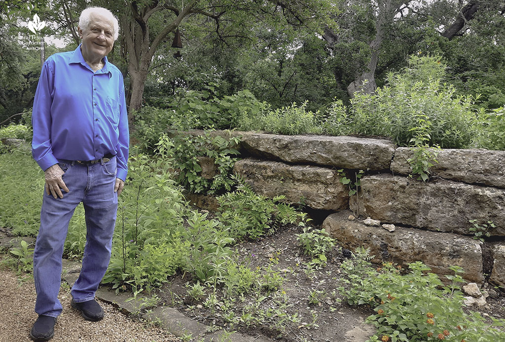 smiling man next to native stone wall and plants 