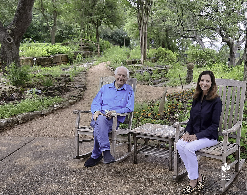 smiling man and woman against sloping woodsy gardens 