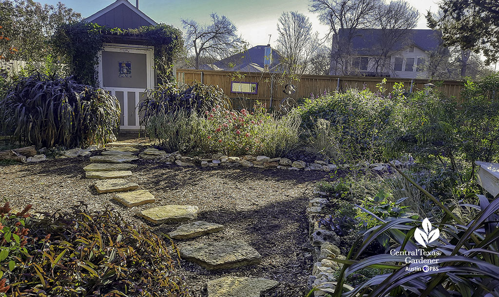 flagstone path on mulch to shed and stone-bordered bed of colorful perennials and grasses