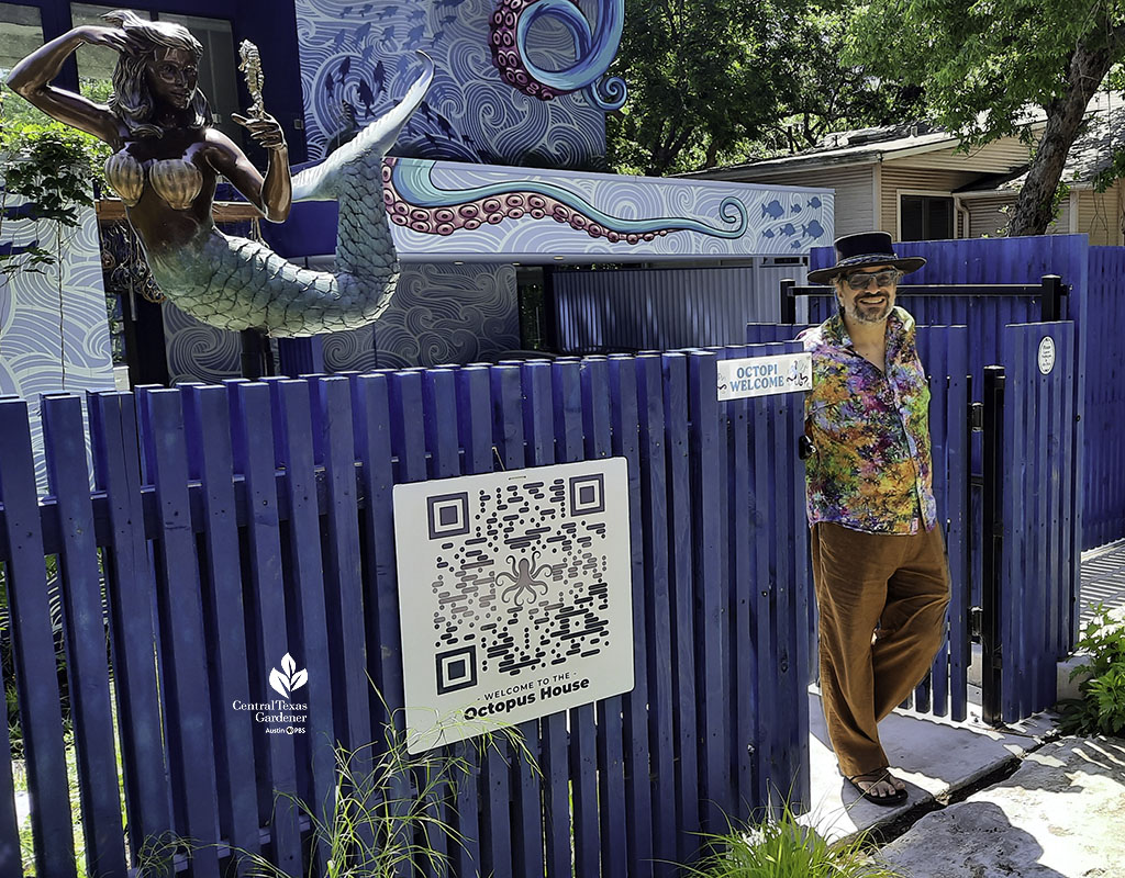 smiling man in tie-dye shirt in front of house painted like an octopus with a mermaid sculpture at front fence