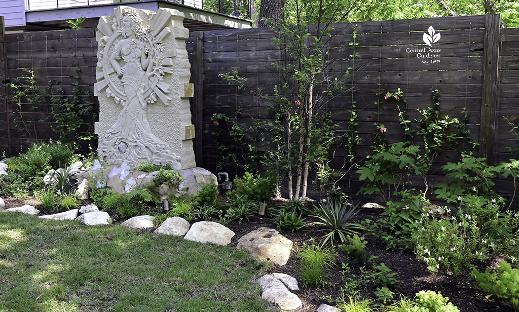 garden bed against fence and life-sized sculpture of a woman 