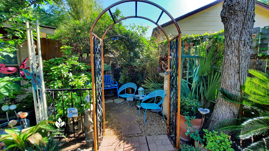 dark orange arbor into secret outdoor room against house and fence featuring blue chairs and blue bench 