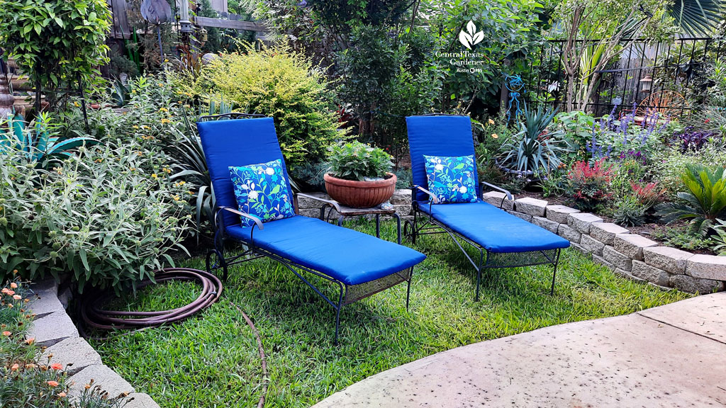 blue chaise lounges on grassy spot next to raised beds of colorful  plants