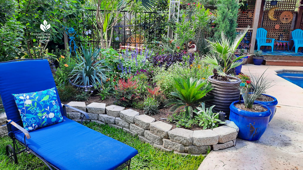 blue chaise lounges on grassy spot next to raised beds of colorful  plants