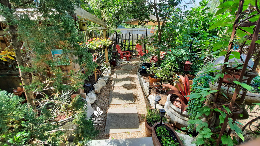 flagstone and gravel path bordered by colorful flowers and foliage plants to red adirondack chairs 