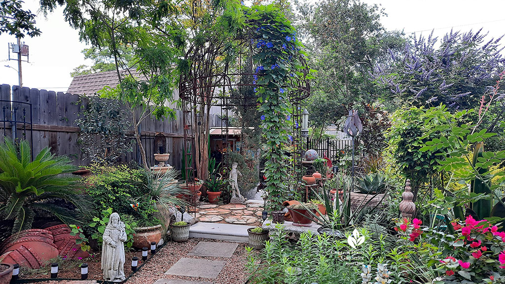 flagstone and gravel path bordered by plants to large iron gazebo and sky blue flowers