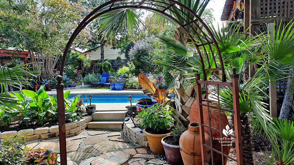 arbor on flagstones bordered by large containers to backyard pool and raised bed gardens