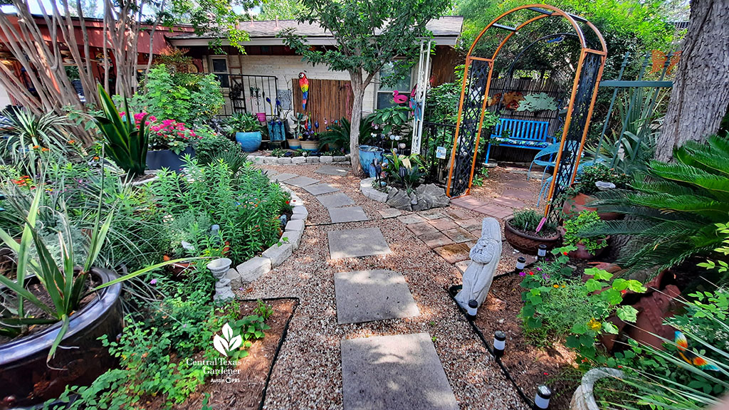 flagstone and gravel path with raised beds and plants on each side ending at orange arbor to secret area against house 