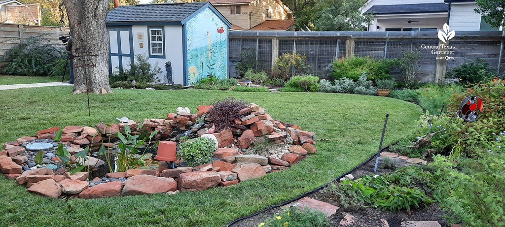 garden beds along fence, small natural stone pond in middle of lawn