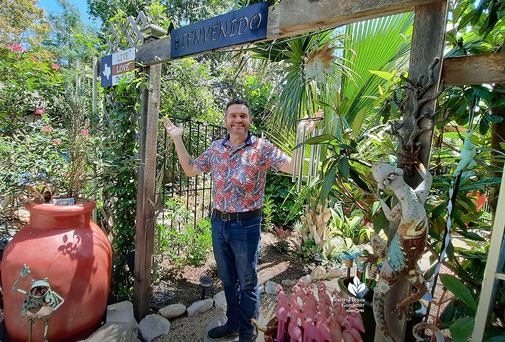 man standing in backyard garden entrance with sign that reads Bienvinedo