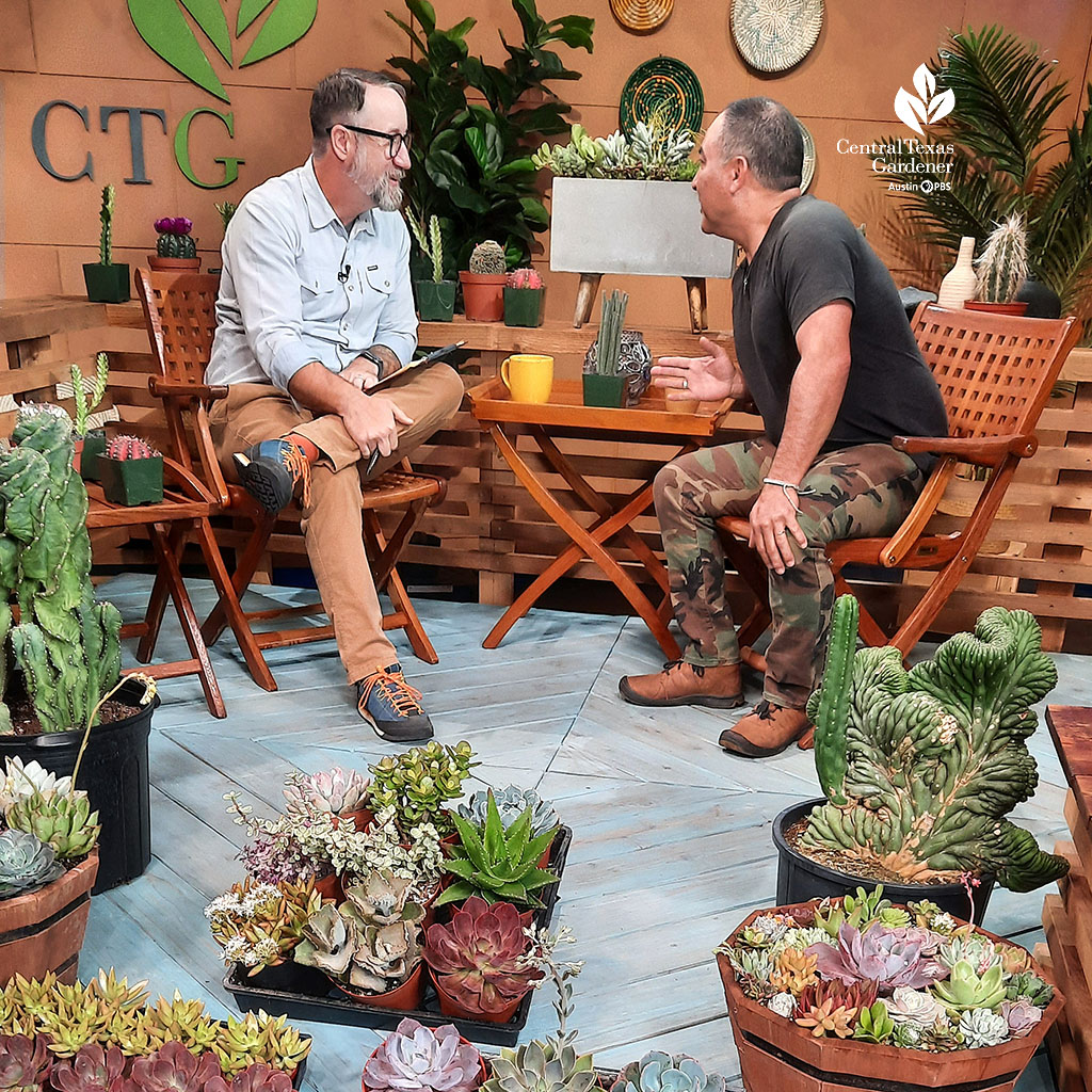 two men on television set with many succulent plants in containers The two are leaning in together and laughing. 