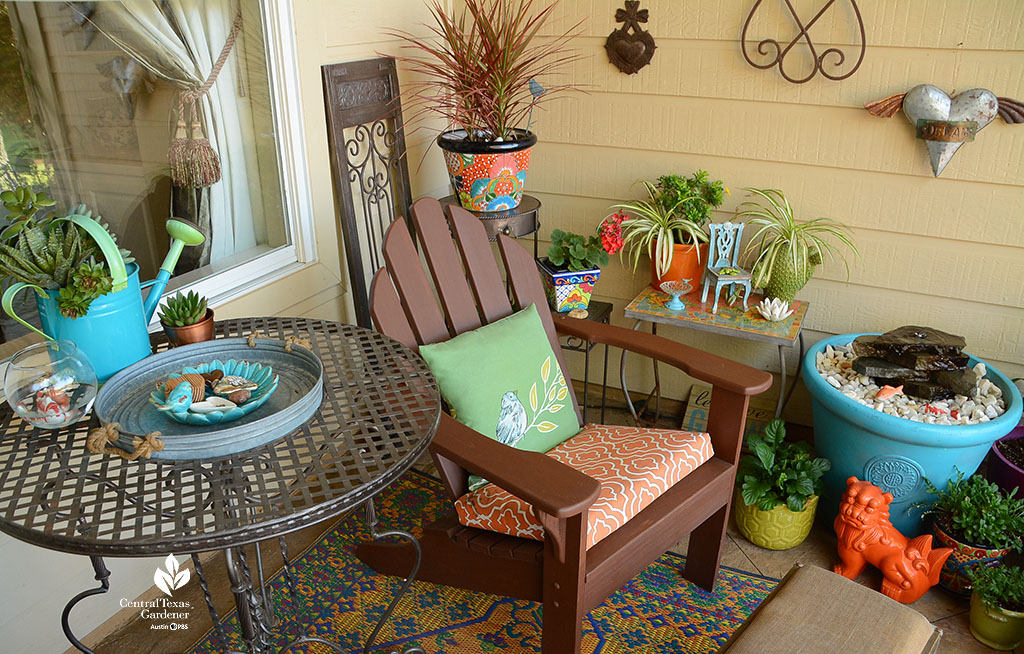 colorful plant containers on patio with adirondack chair and cushion, side table, and artwork on the house walls 