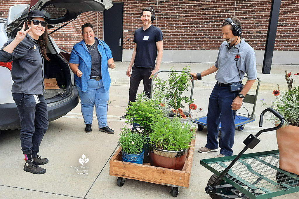 smiling woman at back of open vehicle trunk; carts of plants and 3 crew members (1 woman and 2 men) smiling 