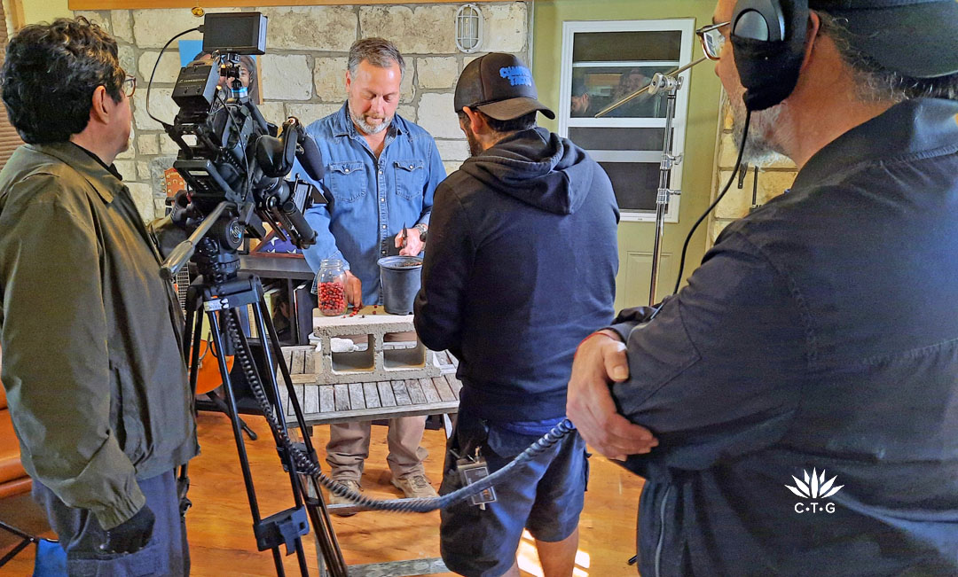 two men with cameras shooting man clipping mountain laurel seeds; man in foreground with headphones