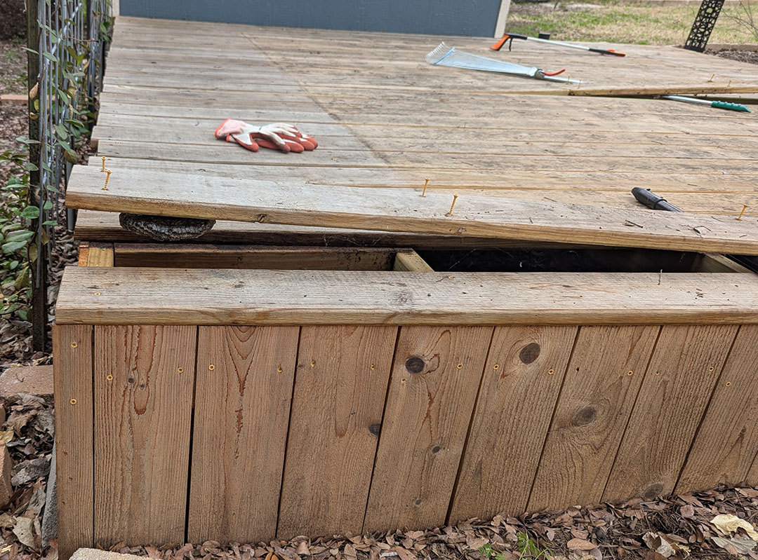 plank of wooden deck pried up to see large hornet nest underneath