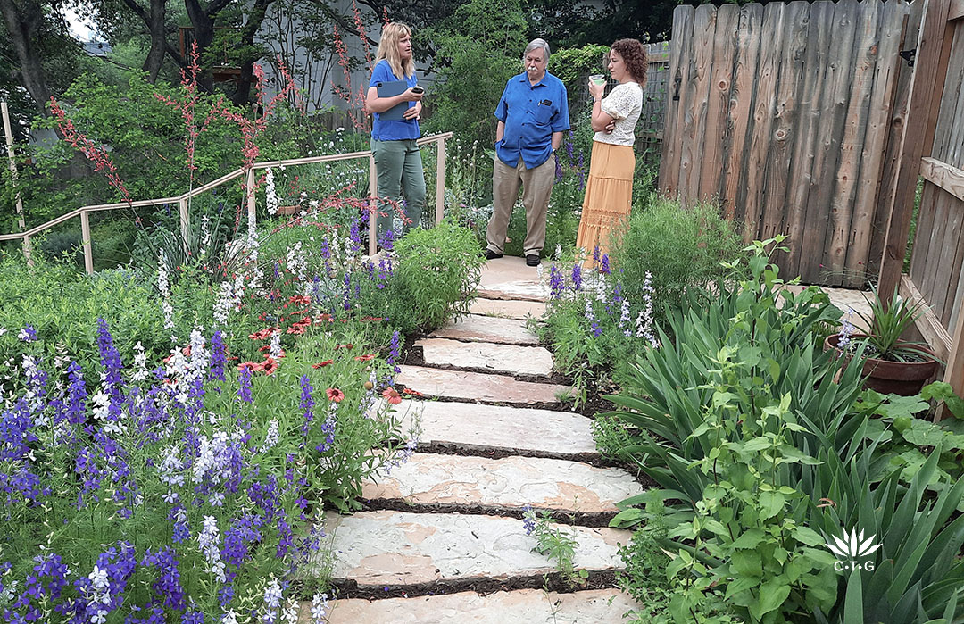 Leah, Roger, and Holly talking along sandstone path bordered by larkspurs