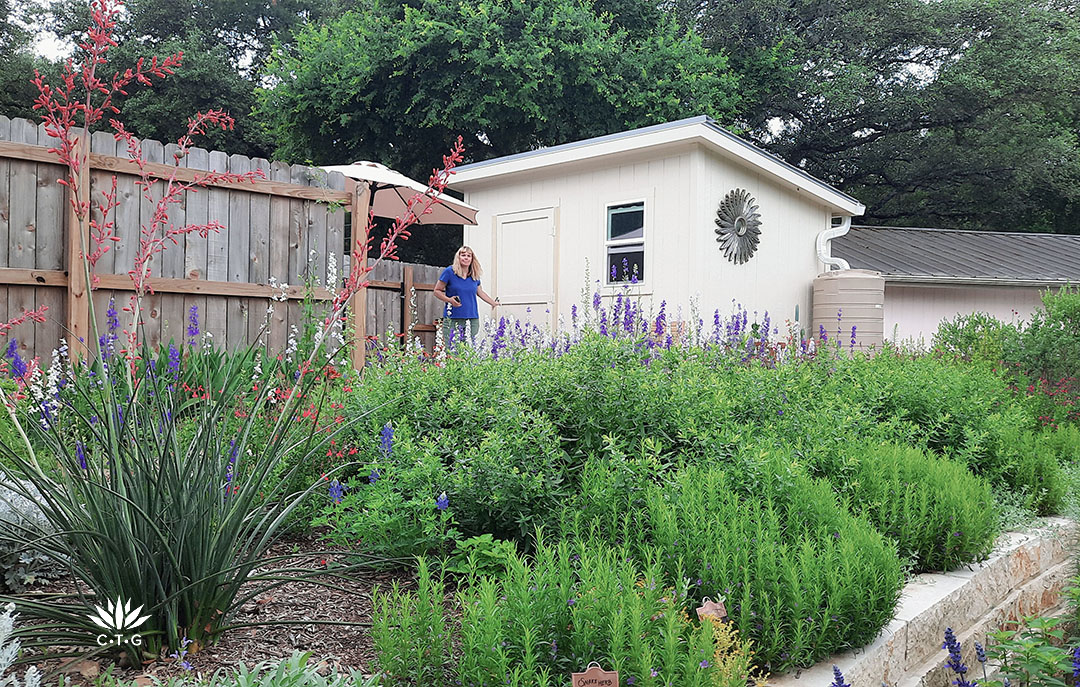 Leah Churner stands next to shed at top of colorful garden