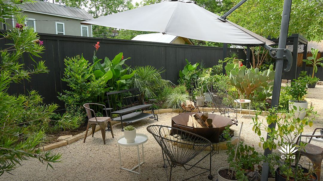 fire pit, bench, and chairs in gravel cove, plants along fence 