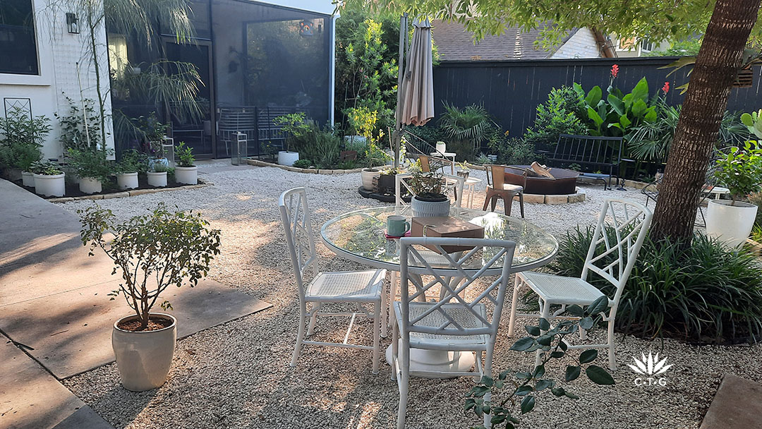 cafe table and chairs on gravel patio in backyard. A screened in porch is framed by small trees and perennials. 