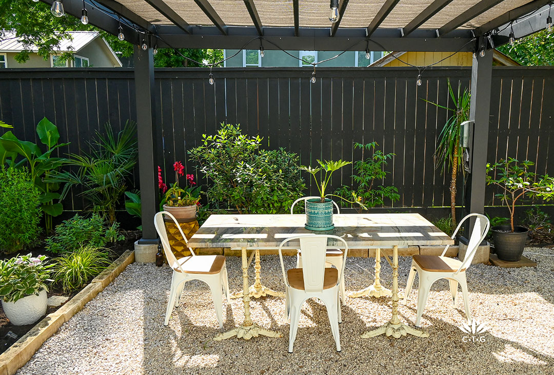 black pergola over dining table; plants along black fence border