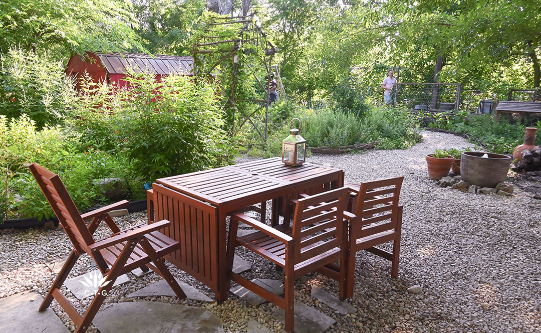 teak dining table and chairs on gravel path a against a garden island bed