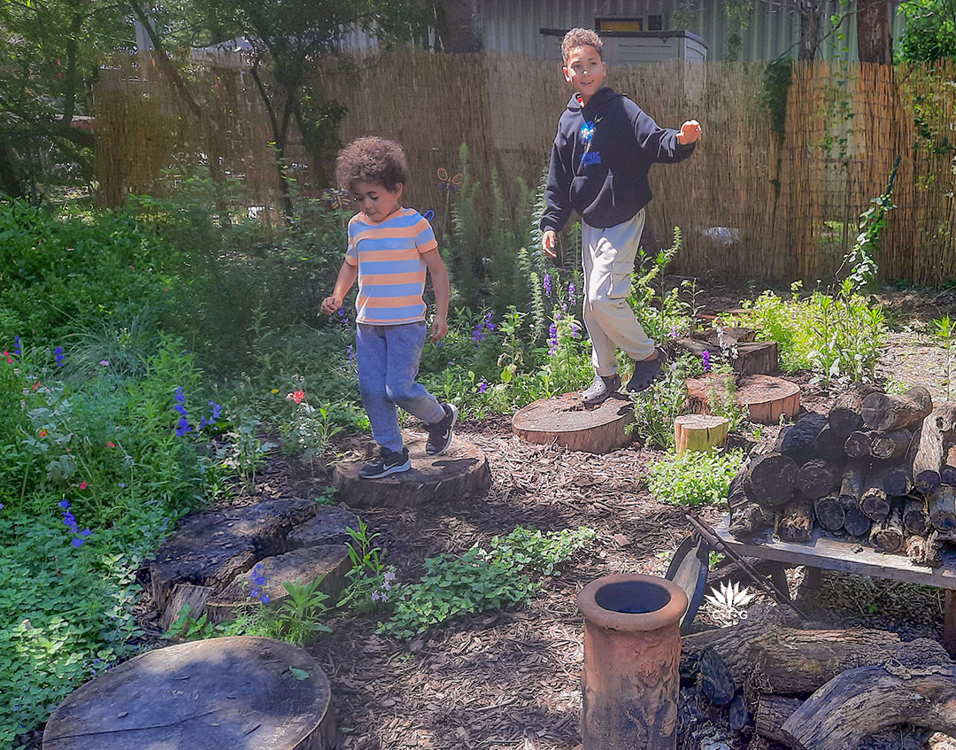 two young boys hopscotching on flat tree stump rounds 